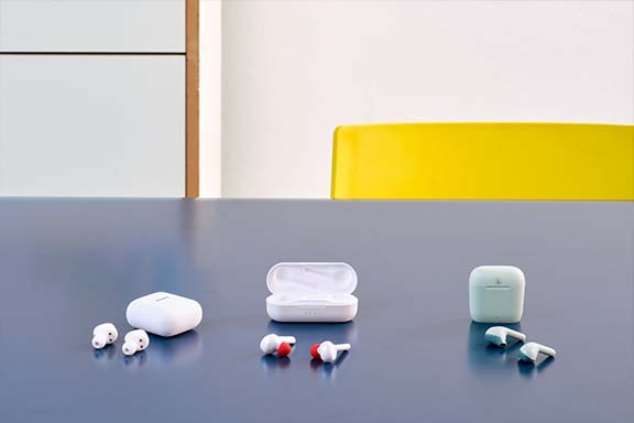 Drei verschiedene kabellose In-Ear-Kopfhörer mit ihren passenden Ladecases liegen auf einem blauen Tisch vor einem minimalistischen Hintergrund.