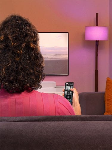 LG-Fernbedienungen Person sitzt auf Sofa und steuert TV mit Fernbedienung.