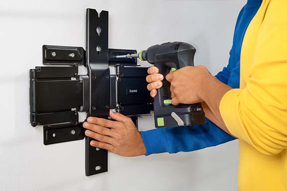 Person schraubt TV-Wandhalterung an Wand fest