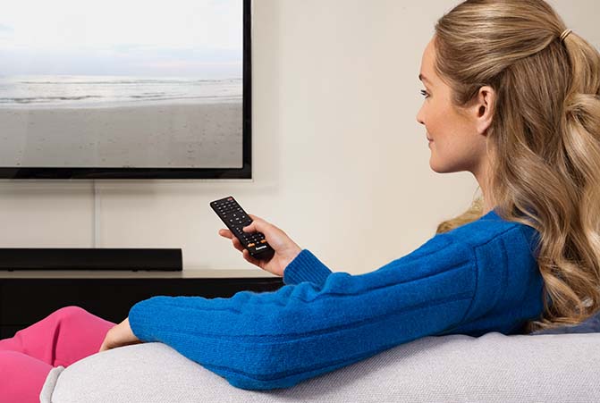 Frau sitzt auf Sofa und schaut Fernsehen mit einer DVB-T2 Antenne.