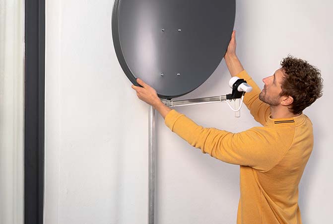 Person richtet eine Satellitenschüssel aus.