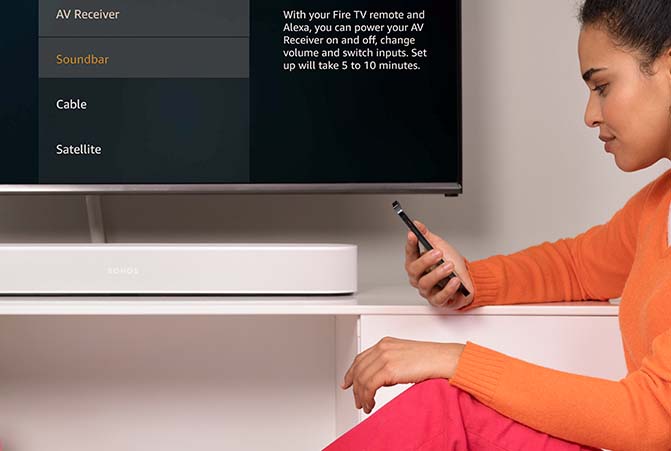 Person hat Handy in der Hand und sitzt vor TV und Soundbar 
