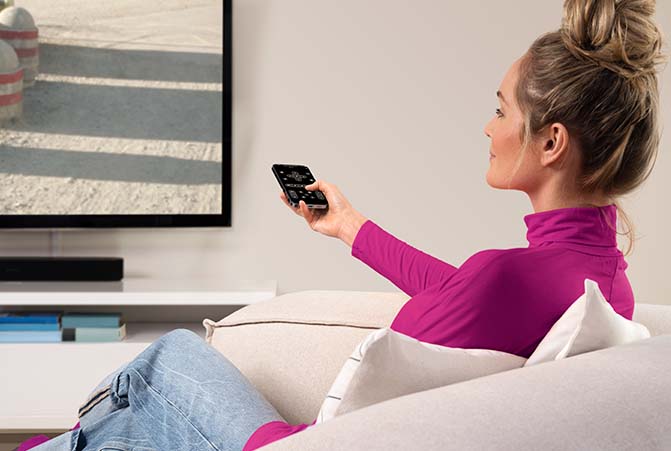 Person sitzt auf dem Sofa und bedient Fernseher mit Handy