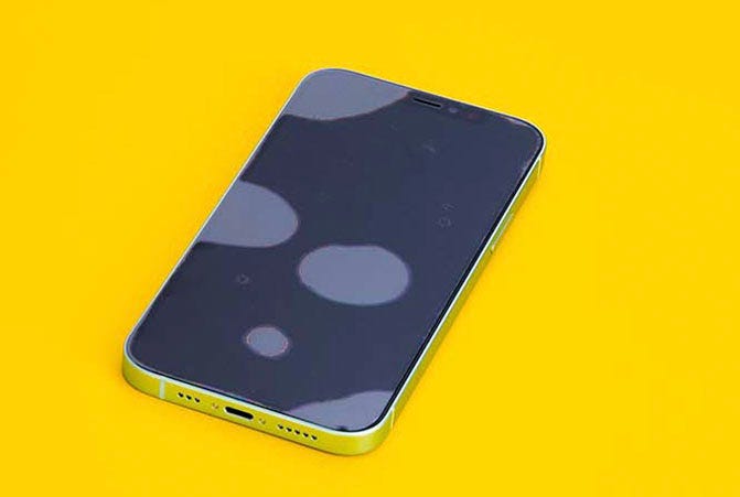 Smartphone liegt auf gelbem Untergrund und das Display ist zum Schutz mit Panzerglas ausgestattet, welches Luftblasen wirft