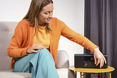 Frau sitzt auf der Couch und nutzt ein Digitalradio von Hama