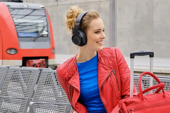 Frau sitzt mit Over-Ear-Kopfhörern am Bahnhof