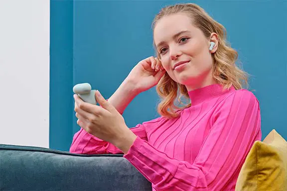 Frau sitzt auf der Couch mit In-Ear-Kopfhörern im Ohr