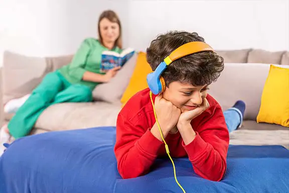 Kind liegt mit Kinderkopfhörern von Hama auf der Couch