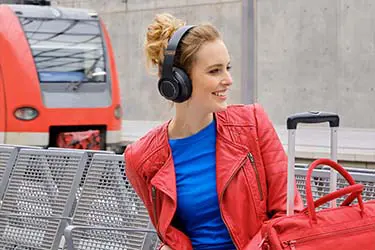 Frau sitzt mit Over-Ear-Kopfhörern am Bahnhof