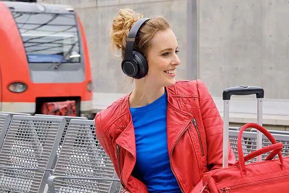 Frau sitzt mit Over-Ear-Kopfhörern am Bahnhof