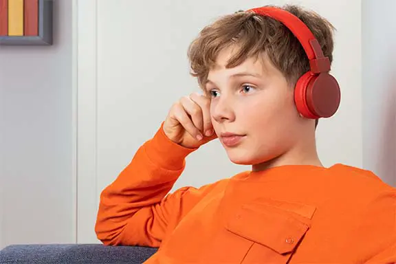 Junge sitzt auf der Couch mit roten On-Ear-Kopfhörern von Hama