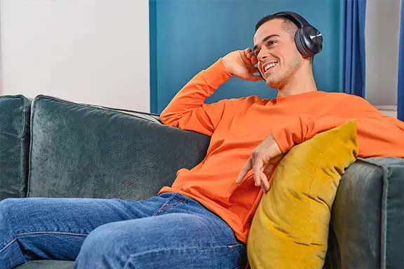 Mann sitzt auf der Couch mit schwarzen Over-Ear-Kopfhörern von Hama