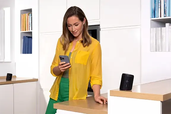 Frau steht mit Handy in der Küche mit Bluetooth-Lautsprecher auf dem Tresen
