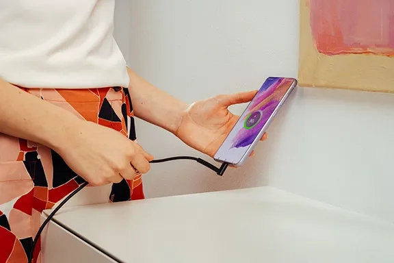 Person hält ein Smartphone in der Hand, das über einen Winkelstecker mit einem USB-Ladekabel verbunden ist.