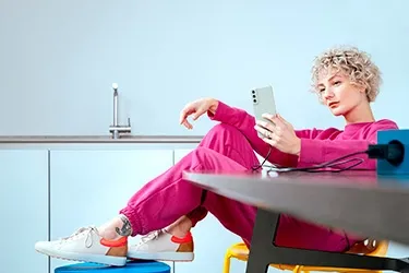 Person sitzt am Tisch und lädt ein Samsung Smartphone mit einem Ladekabel von Hama.
