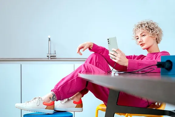 Person sitzt am Tisch und lädt ein Samsung Smartphone mit einem Ladekabel von Hama.