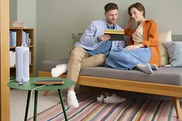 iPhone liegt auf einem induktiven Ladegerät und wird geladen. Im Hintergrund sitzen zwei Personen auf einem Sofa