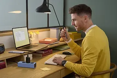 Person sitzt am Schreibtisch, während ein Smartphone mit einem Schnellladekabel aufgeladen wird.