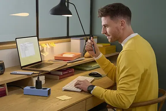 Person sitzt am Schreibtisch, während ein Smartphone mit einem Schnellladekabel aufgeladen wird.