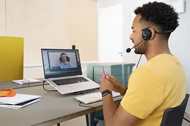 Person sitzt mit Headset am Laptop im Home Office