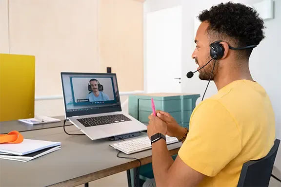 Person sitzt mit Headset am Laptop im Home Office