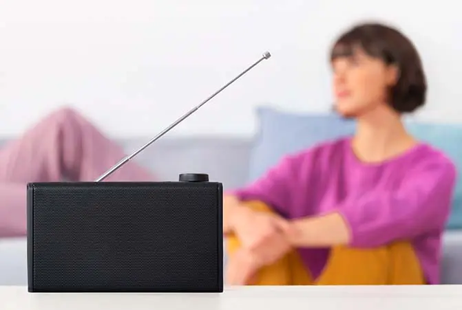 Schwarzer Hama UKW-Radio im Vordergrund, eine Person in Wohnumgebung im Hintergrund.