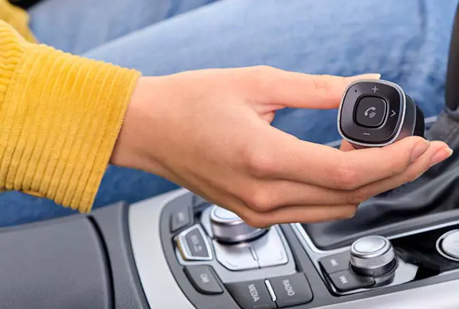 Person sitzt im Auto und hält einen Bluetooth-Reveiver für Kfz in der Hand.