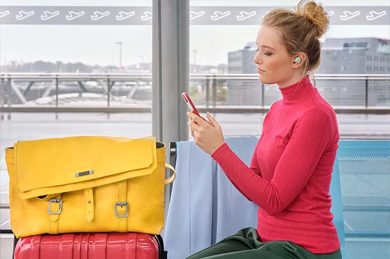 Alle Infos rund um Bluetooth-Geräte im Flugzeug Person mit Bluetooth-Kopfhörer von Hama hält ein Smartphone in der Hand.