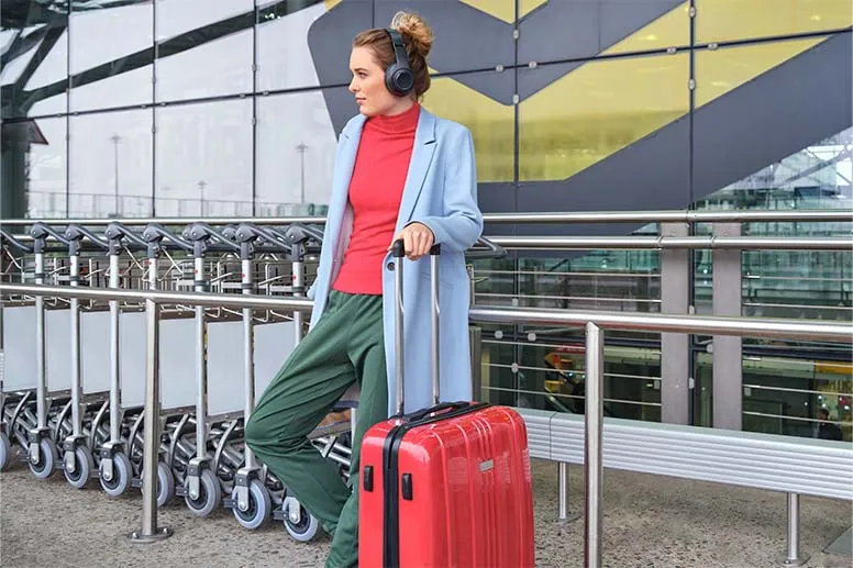 Frau steht mit Koffer und Over-Ear-Kopfhörern vor Einkaufswägen