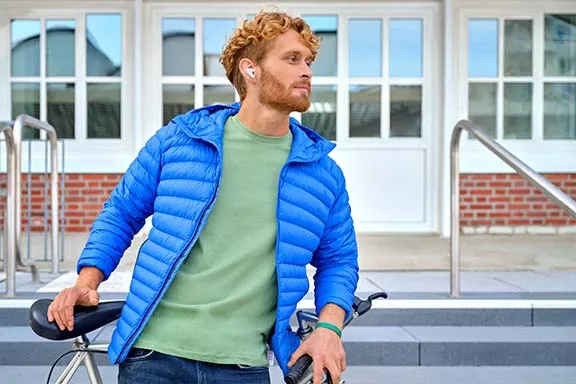Mann neben Fahrrad von Gebäude schaut nach rechts mit Bluetooth In-Ear-Kopfhörern im Ohr