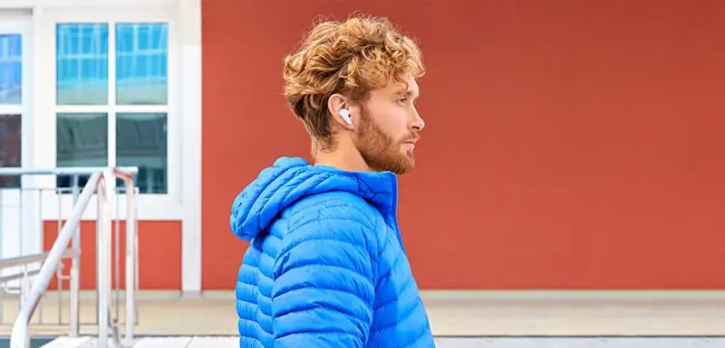 Mann mit blauer Jacke an einer Treppe mit kabellosen Bluetooth-Kopfhörern