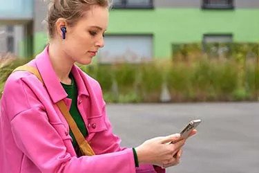Frau mit pinker Jacke bedient ein Smartphone und trägt Earbuds