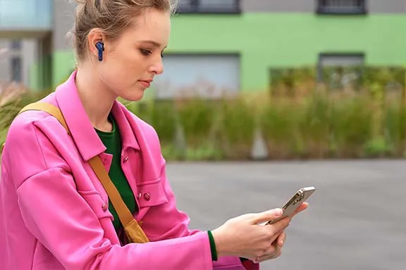 Frau mit pinker Jacke bedient ein Smartphone und trägt Earbuds