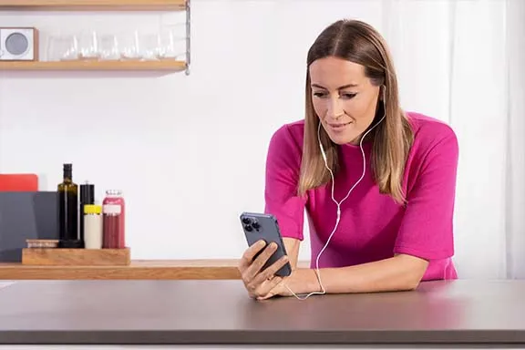 Frau mit pinkem Oberteil bedient Smartphone und hat kabelgebundene Kopfhörer