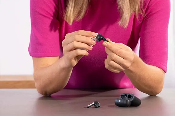 Frau reinigt mit einem Tuch ihre schwarzen Earbuds