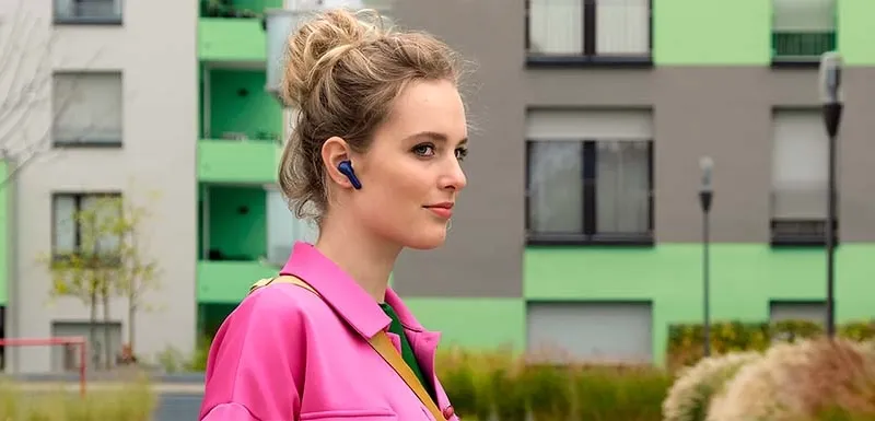 Frau mit pinkem Oberteil schaut nach rechts schauend und trägt schwarze Earbuds