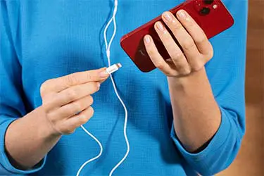 Kabelgebundenes Telefonieren mit dem Smartphone. Person steckt ein Headset-Kabel in ein Smartphone ein.