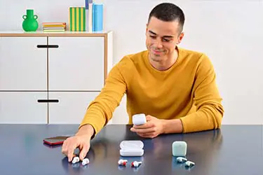 Vergleich kabelloser In-Ear-Kopfhörer. Mann sortiert mehrere kabellose In-Ear-Kopfhörer mit Ladecases auf einem Tisch.