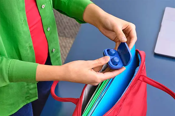 Kabellose In-Ear-Kopfhörer für unterwegs. Person packt ein kabelloses In-Ear-Kopfhörer-Set in einer blauen Ladebox in eine Tasche.