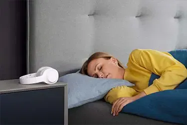 Person und Over-Ear Kopfhörer daneben auf dem Nachttisch.