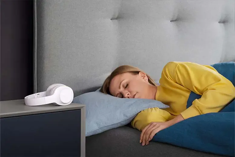 Person und Over-Ear Kopfhörer daneben auf dem Nachttisch.