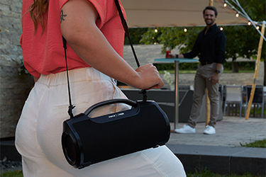 Hama Mate Pro Frau trägt Hama Bluetooth-Lautsprecher Mate Pro am Tragegurt auf einer Gartenparty