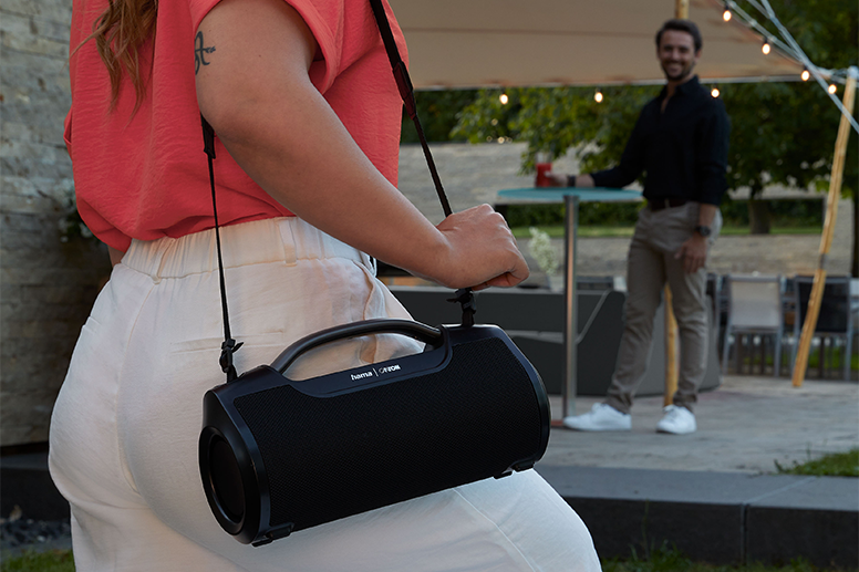 Hama Mate Pro Frau trägt Hama Bluetooth-Lautsprecher Mate Pro am Tragegurt auf einer Gartenparty