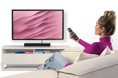 Person sitzt auf Sofa und bedient Fernseher mit Fernbedieunung