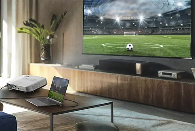 Wohnzimmer mit TV-Gerät auf dem ein Fußballspiel läuft, davor ein Laptop auf einem Tisch