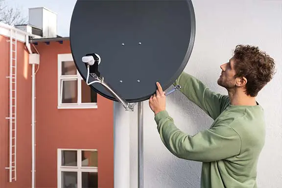 Mann montiert eine Satellitenschüssel an einer Hauswand und richtet diese aus