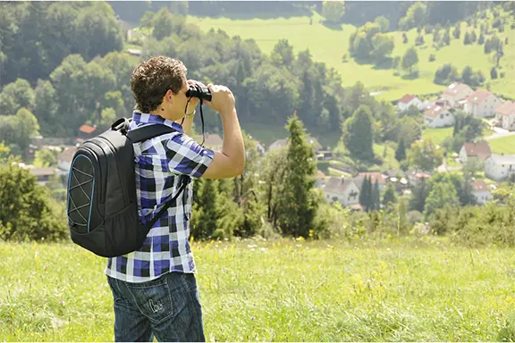 Person steht auf Almwiese mit Fernglas