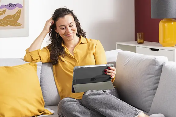 Person sitzt mit Tablet auf dem Sofa, Tablet ist in Tablethülle