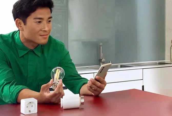 Mann sitzt mit Smart Home Steckdosen und Glühbirne am Tisch.