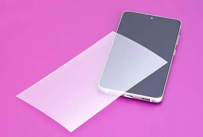 Displayschutzfolie von Hama liegt schräg über einem weißen Smartphone auf einem pinken Untergrund